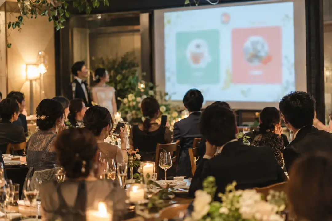 結婚式二次会で、会場後方のスクリーンにaunicoのゲーム画面が投影されている様子